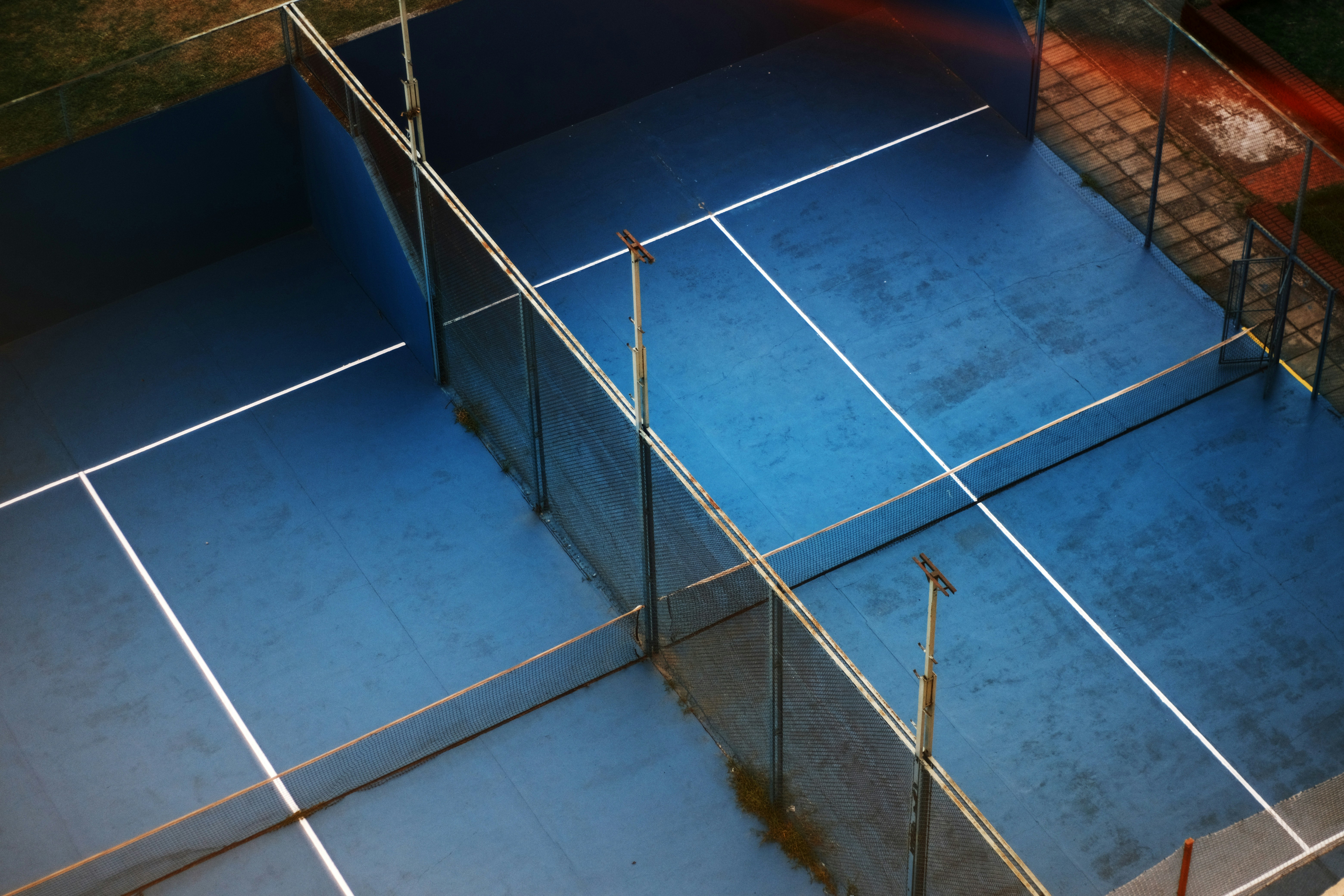 Vogelperspektive eines leeren, blauen Padelplatzes in urbaner Umgebung, umgeben von Maschendrahtzäunen, die zu einem dynamischen Spiel einladen